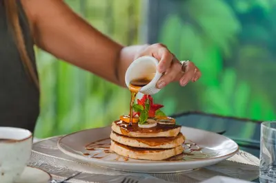 a person pouring syrup onto a stack of pancakes at Hotel Sanctuarium in Fortuna