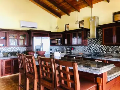 a kitchen with wooden cabinets and a large island with chairs at Rancho RachMare in Playa Coyote, a Beach Home! in Nandayure