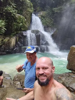 two men sitting on rocks in front of a waterfall at La Ceiba Biolgical Reserve in Platanillo