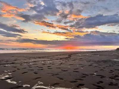 a sunset on a beach with footprints in the sand at Luxury Oceanfront Penthouse w Loft and 2 Balconies in Bejuco