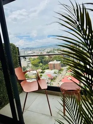 a balcony with a pink chair and a palm tree at Spectacular view and comfort from the 21st floor in San José
