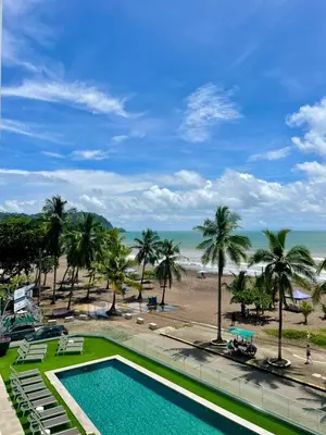a swimming pool next to a beach with palm trees at Pacific Point - Pure Vida in Jaco, Costa Rica in Jacó