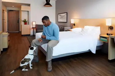 a man sitting on a bed with a dog next to him at Hyatt Place Cariari/Convention Center in San José