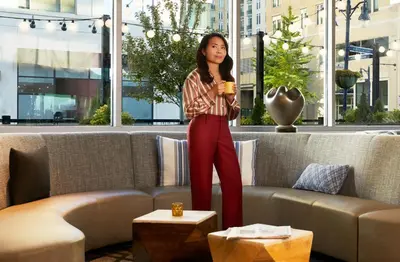 a woman standing next to a couch holding a cup of coffee at Hyatt Place Cariari/Convention Center in San José