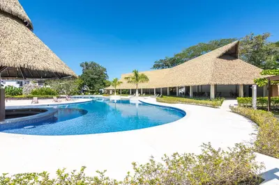 a swimming pool with thatched umbrellas at a resort at Relaxing Beach Oasis - Gated Community with Pool - Mini Golf - Walking Distance to Beach in Jacó