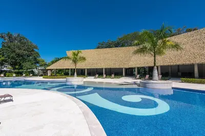 a swimming pool with a resort building and palm trees at Relaxing Beach Oasis - Gated Community with Pool - Mini Golf - Walking Distance to Beach in Jacó
