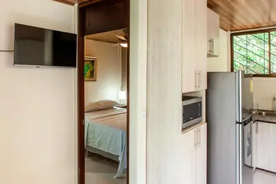 a room with a bed and a kitchen with a refrigerator at Nosara Beach Cabins in Nicoya