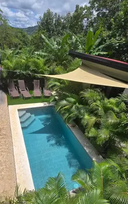 a swimming pool with chairs and palm trees at Casa Cascada La Roca in Sámara