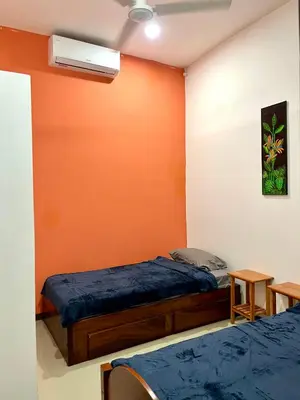 a bedroom with two beds and an orange wall at Pura Vida Stay Liberia in Liberia