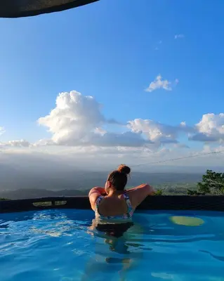 a woman sitting in a swimming pool in the sky at Hygge House with a view of the Arenal Volcano and the San Carlos Plain in Vieja