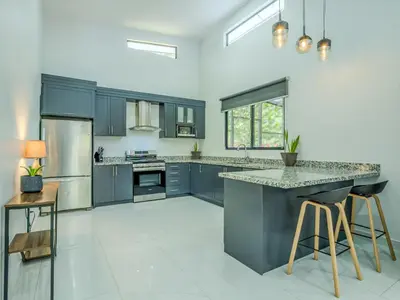a kitchen with blue cabinets and a counter with stools at Modern Retreat in the Rainforest with River Access in Ojochal