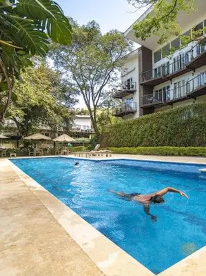 a man swimming in a swimming pool next to a building at Apartamento moderno con vista al río, piscinas y gym Costa Rica in Santa Ana