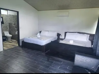 a bedroom with two beds and a bathroom with a toilet at Pino Lodge, Río Celeste in Upala