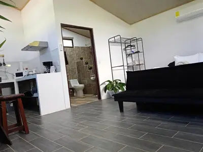 a living room with a black couch and a kitchen at Pino Lodge, Río Celeste in Upala