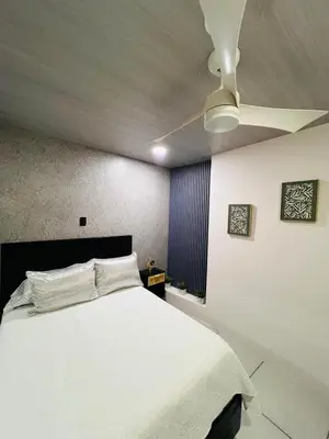 a bedroom with a white bed with a ceiling fan at Kens Lower department in Quepos