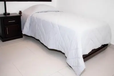 a bed with a white comforter and a night stand at Casa PAMPA in Liberia