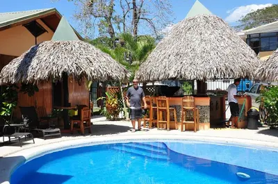 a man standing next to a swimming pool with two straw umbrellas at Poolside Unit at Beachfront Hotel in Sámara
