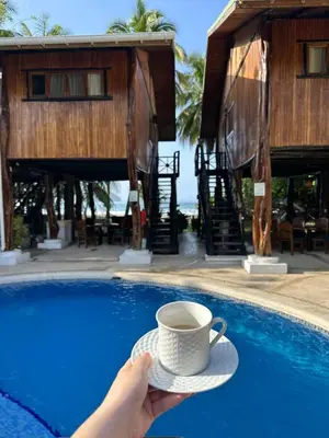 a person holding a cup of coffee next to a pool at Tree House Inn Ocean Front Unit #2 in Sámara