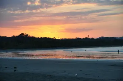 a sunset on a beach with people in the water at Samara Tree House Inn Unit 4 in Sámara