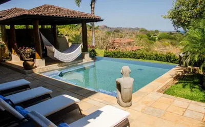 a swimming pool with a statue next to a hammock at Casa Serena Luxury Retreat in Reserva Conchal in Brasilito