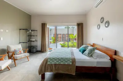 a bedroom with a bed and a chair and a window at Calathea Arenal Villa in Agua Azul