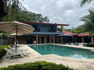 a house with a swimming pool with two chairs and an umbrella at Casa Lapa Herradura Completa in Herradura