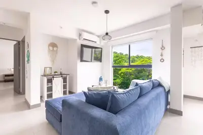 a blue couch in a living room with a window at Playa Mantas - 7th Floor - Sea View - Beach Club Access - Balcony - Beach in Punta Leona