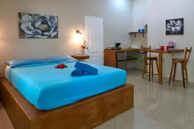 a bedroom with a bed with blue sheets and a kitchen at Playa Negra Surf Lodge in Playa Negra