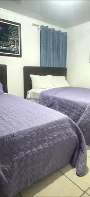 two beds in a hotel room with purple sheets at Rohrmoser a 100 metros de la embajada americana in San José