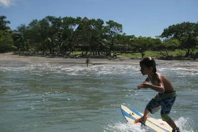 a young boy on a surfboard in the water at Hotel Playa Negra in Playa Negra