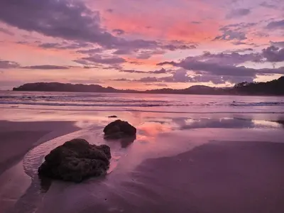 a sunset on a beach with rocks in the sand at Screened-In Porch! Short Walk To Beach! in Sámara
