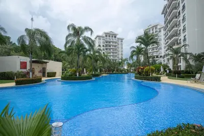 a large blue swimming pool with palm trees and buildings at Jaco Bay 4303 in Jacó
