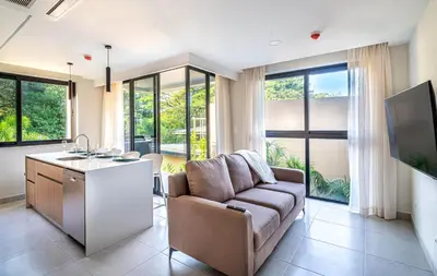 a living room with a couch and a kitchen with windows at Torres del Mar 1202 in Jacó