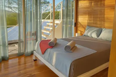 a bedroom with a bed and a balcony with sliding glass doors at luxury wooden house mountain view in Hojancha
