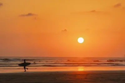 a person holding a surfboard on the beach at sunset at New! 5-Min Walk to Surf - Private Pool - 2BR in Playa hermosa