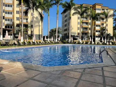 a large swimming pool with palm trees and buildings at CL127 Modern Penthouse in Jacó