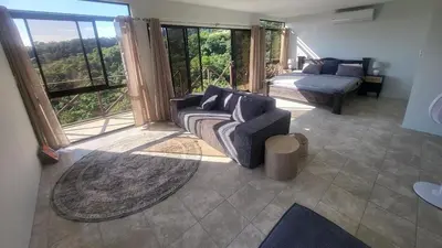 a living room with a couch and a bed and windows at Casa Pura Vista in Playa Hermosa