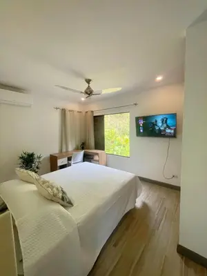 a bedroom with a white bed and a tv on the wall at Tesoro Escondido in Naranjito