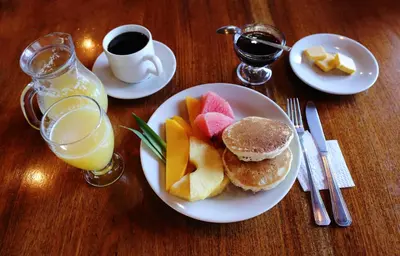 a plate of food with pancakes and fruit and a cup of coffee at Hotel El Atardecer in Monteverde Costa Rica