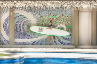 a person holding a surfboard in front of a mural at Olas Verdes Hotel in Nosara