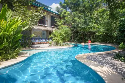 a swimming pool in front of a house with two people in it at Olas Verdes Hotel in Nosara