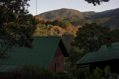 a red barn with a green roof and mountains in the background at Cedrela Eco-Lodge & Restaurante in El Copey