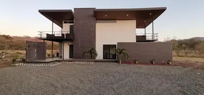 a house on a gravel lot with palm trees in front of it at Playa Potrero in Potrero