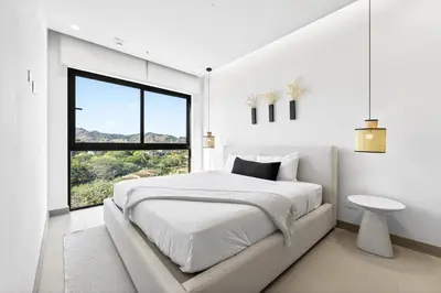 a white bedroom with a large bed and a window at Tropics at Naumi, Ocean Views, Gym & Pools in Sardinal