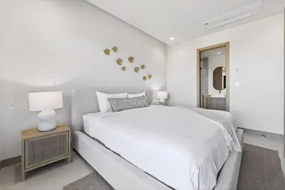 a white bedroom with a bed and a night stand at Tropics at Naumi, Ocean Views, Gym & Pools in Sardinal