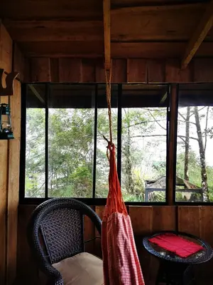 a hammock hanging in a room with a table and windows at Rio Paquita Lodge in Tapantí