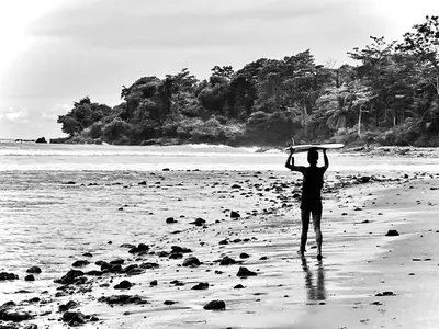 a man holding a surfboard on a beach at New Beachfront Jewel in the Jungle on Golfo Dulce in Tapantí