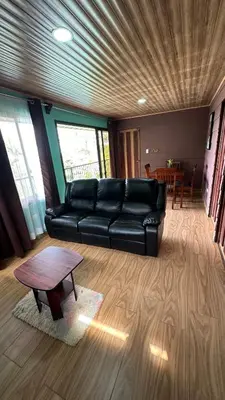 a living room with a black leather couch and a table at Villa Solevila in Turrialba