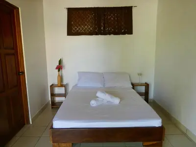 a bedroom with a bed with white sheets and a window at La Buena Vida in Nicoya