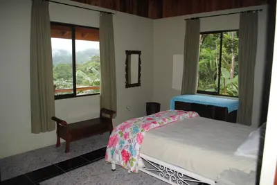 a bedroom with a bed and two windows with a view at Toucan Villa in Caña Blanca